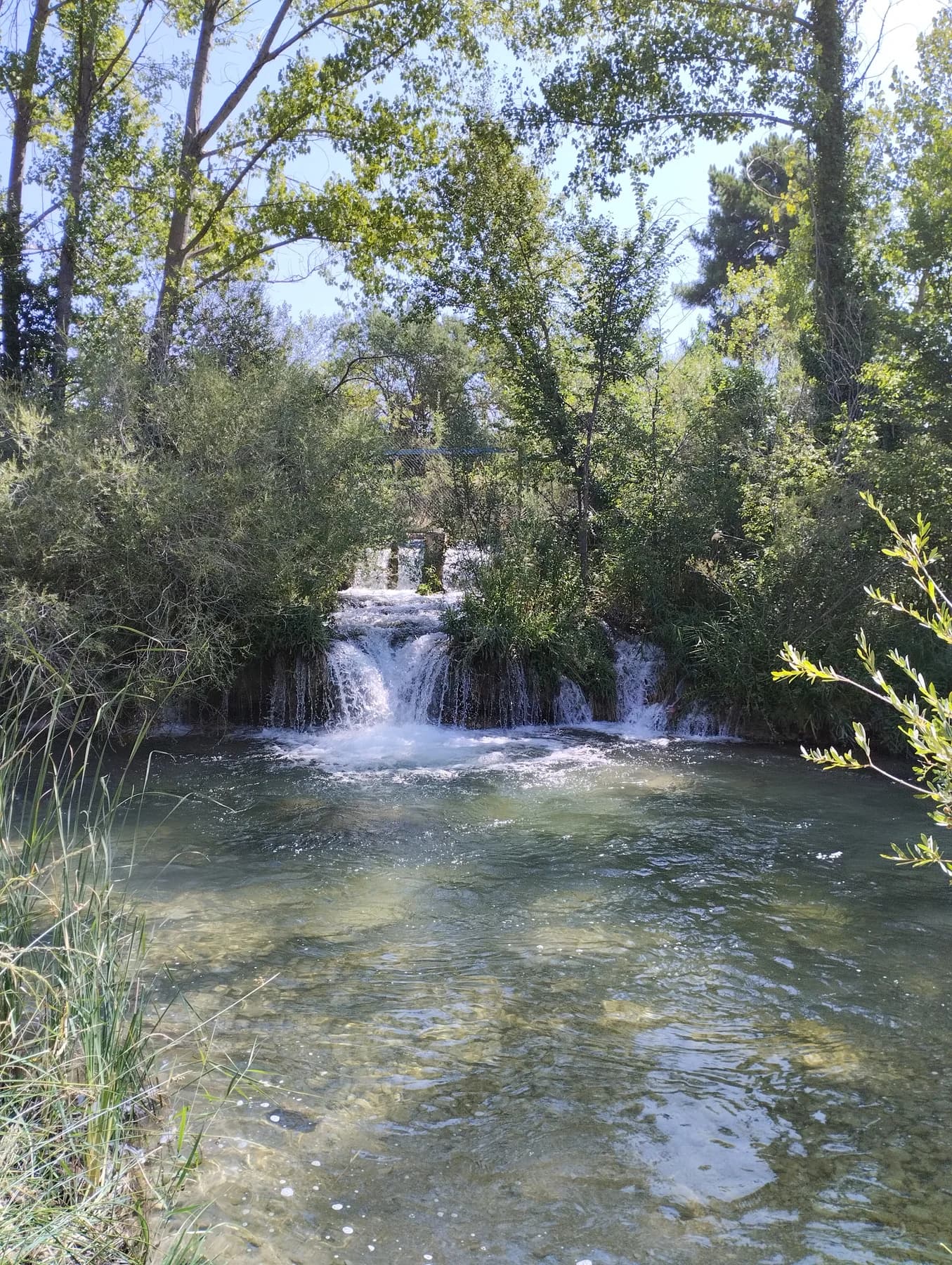 Cascada iluminada por el sol entre árboles junto al río Júcar